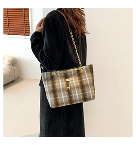Detail view of plaid tote bag with golden chain strap and deer pendant on model