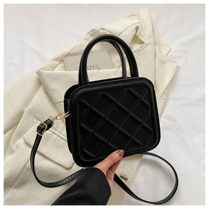 Detailed close-up of black quilted texture on square handbag with gold hardware
