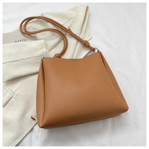 Close-up of brown faux leather tote bag with cylindrical straps and knot detail on white fabric