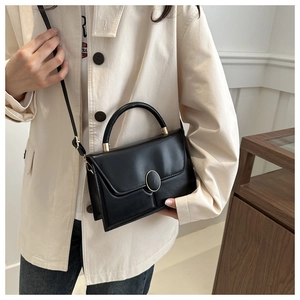 Detail of black matte leather square bag with gold oval clasp and adjustable strap