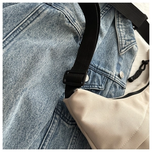 Close-up of beige canvas crescent bag with black adjustable strap on blue denim