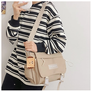 Gros plan d'un sac messager kaki avec écusson logo blanc et breloque en peluche mignonne