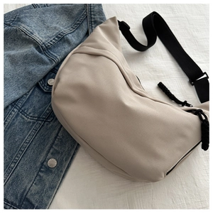 Detail of a beige crescent moon crossbody bag with adjustable black strap on denim jacket