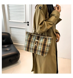 Detail van geruite tweed shopper met gouden ketting en hertenhanger op een beige trenchcoat