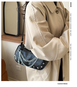 Détail du sac noir à motif pierre avec chaînes argentées sur un trench-coat beige