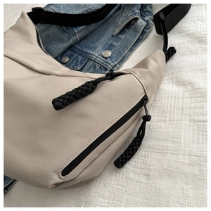 Close-up of beige canvas dumpling bag with black woven rope zipper pull and wide strap