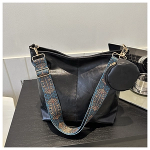 Detail of black leather hobo bag featuring bohemian wide strap and a small coin purse charm