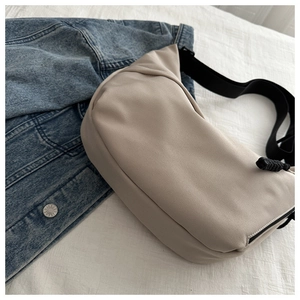 Detail of beige crescent bag on white bedding with a blue denim jacket