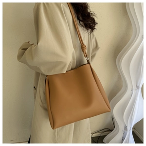 Detail of light brown tote bag featuring decorative knot shoulder strap and metal ring