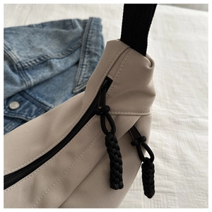 Close-up of beige canvas dumpling bag with black zipper detail and rope puller