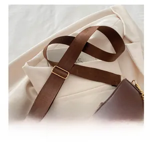 Detalle de la correa ancha de tejido y hebillas doradas en el bolso retro marrón