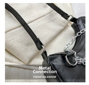 Détail de la boucle en métal et chaîne argentée sur sac noir à motif crocodile
