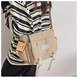 Détail du sac messager beige en nylon avec boucle de fermeture et charme en peluche toast