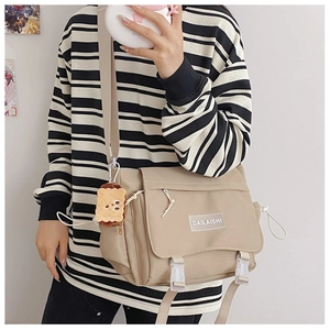 Détail du sac messager en nylon beige avec boucles en plastique et un charmant pendentif biscuit