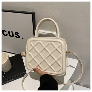 Detailed view of cream quilted square handbag with metal clasp and top handle texture
