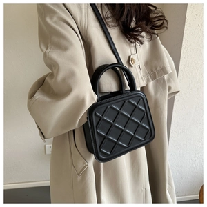 Elegant black quilted crossbody bag with top handle shown on a model in beige coat