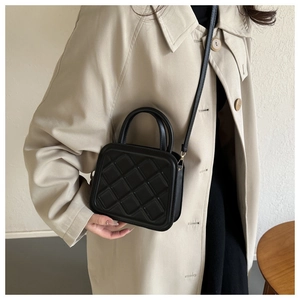 Close-up of black quilted crossbody bag with top handles on a model in a beige coat