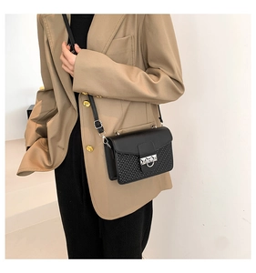 Detail of black woven crossbody bag with silver ring buckle on a beige blazer