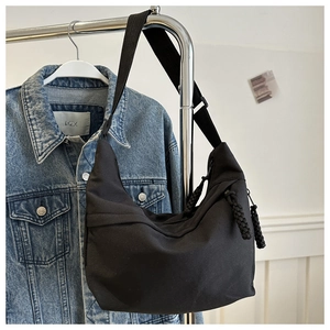 Detail of black crescent hobo bag with wide shoulder strap and woven zipper puller