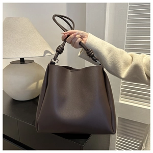 Detailed shot of dark brown leather tote bag showing rope knot strap and metallic rings