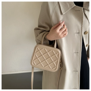 Detail of beige quilted square handbag with embossed texture and crossbody strap