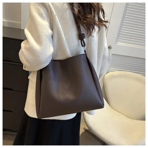 Detailed view of dark brown leather tote bag with knot strap detail on white coat