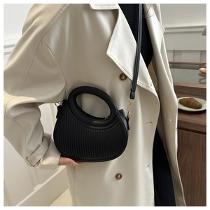Nahaufnahme der schwarzen Textur-Handtasche mit Goldhaken getragen zu einem beigen Mantel