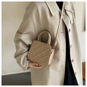 Detail of beige quilted crossbody bag with top handle shown on a stylish trench coat