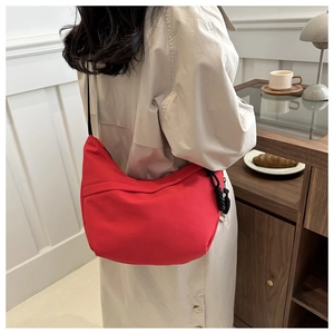 Detailed back view of a red crescent canvas shoulder bag worn by a model in a cafe setting