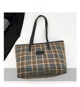 Detail of plaid tote bag with brand logo patch and leather trim finishing