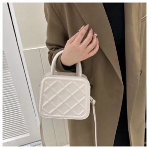 Close-up of beige quilted square handbag with metal buckles and crossbody strap