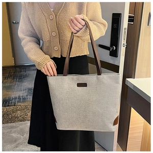 Close-up of canvas tote bag with brown leather handles and a fashion label detail