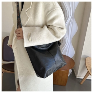 Detail of black leather tote bag with retro ethnic pattern wide strap on white coat