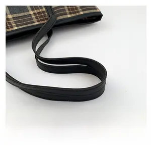 Detail of checkered tote bag featuring textured black leather handle and vintage plaid pattern