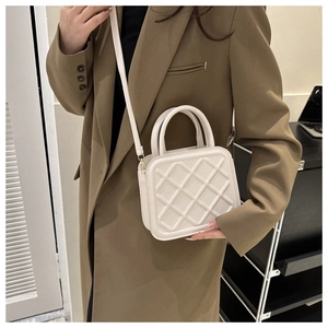 Detail view of a white quilted crossbody bag with a refined top handle and clean finish