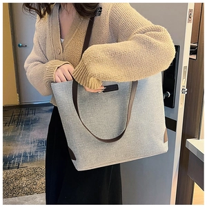 Detail of grey canvas tote bag with brown straps and fashion label on front