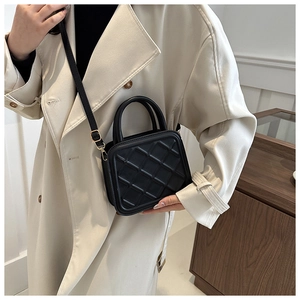 Detail of black quilted mini bag featuring dual top handles and gold hardware details