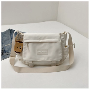 Détail du sac messager crème en nylon avec boucle et breloque peluche en forme de biscuit