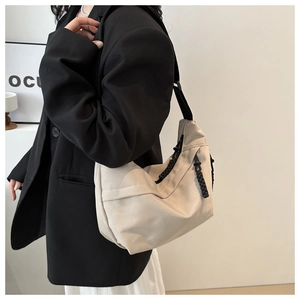 Detailed view of beige canvas dumpling bag with black adjustable strap on model