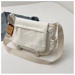 Détail du sac messager en nylon blanc cassé avec boucles réglables et un pendentif peluche