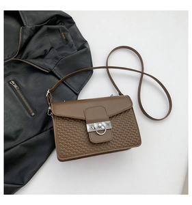 Close-up of brown leather crossbody bag with woven texture and silver metal ring clasp
