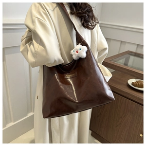 Detail of dark brown oil-wax leather shoulder bag with a white plush cloud charm