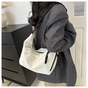 Detail of minimalist cream dumpling bag with wide black strap and woven zipper pull