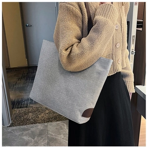 Detail of grey canvas tote bag with brown leather corner patch and textured finish