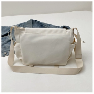Détail du sac messager en nylon blanc crème avec bandoulière large et poches latérales utiles