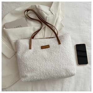 Gros plan sur le sac fourre-tout en polaire blanche avec anses en cuir marron et écusson