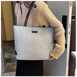 Detail of grey woven tote bag with brown leather straps and fashion label decoration