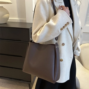 Minimalist large brown matte leather tote bag worn by model in cozy interior scene