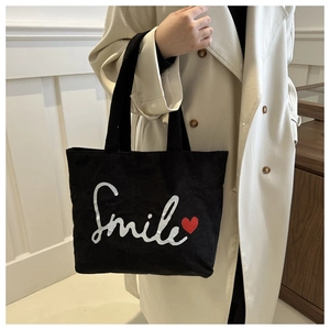 Detail of black corduroy tote bag featuring white Smile text and red heart graphic