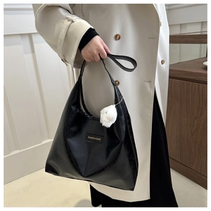 Detail of black PU leather hobo bag with fashion label and white plush ball charm